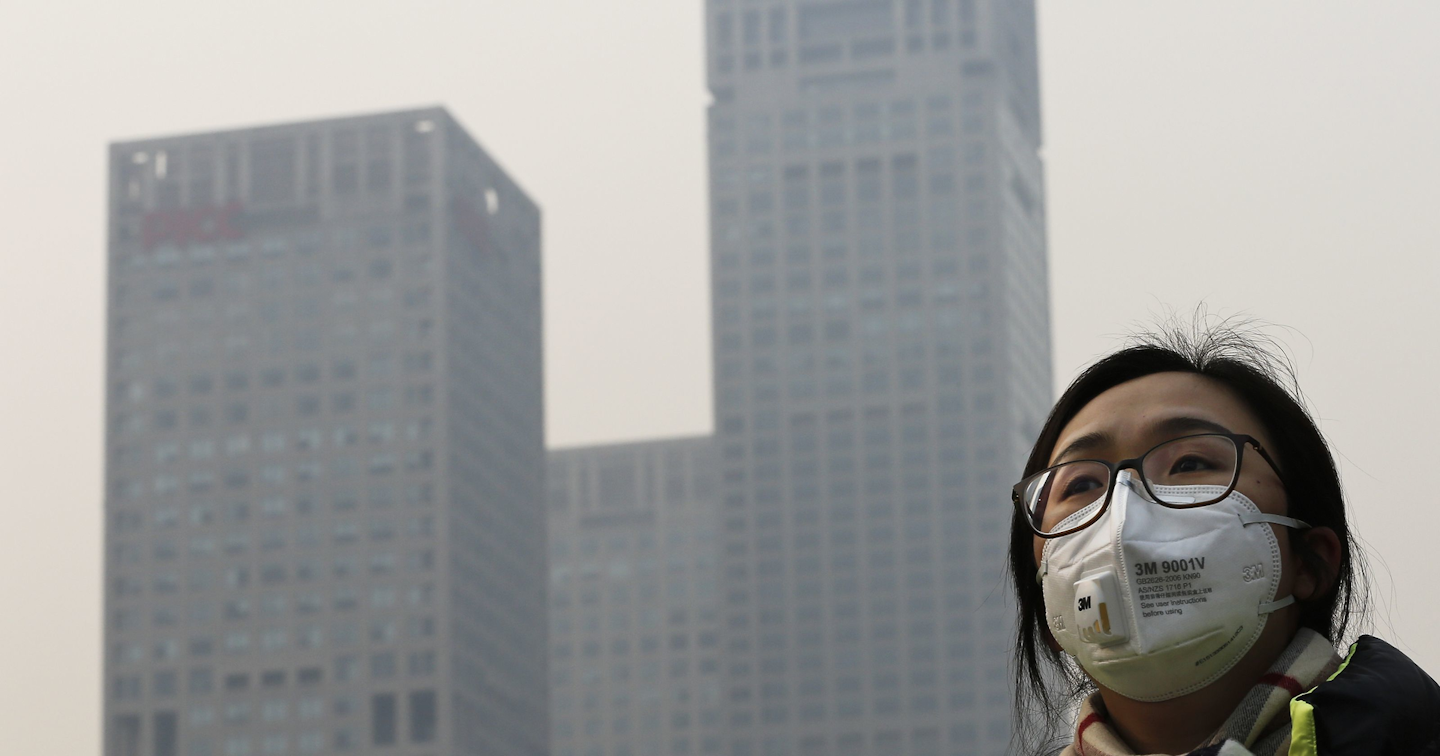 A woman wearing a face mask to protect herself from pollutants walks past office buildings shrouded with pollution haze in Beijing, Monday, Dec. 7, 2015. (AP Photo/Andy Wong)
