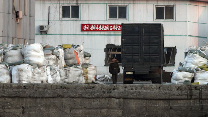 A North Korean soldier walks past a truck park near the goods pile up on a dockyard in Sinuiju, North Korea, as seen from Dandong in northeastern China's Liaoning province. (Chinatopix via AP)