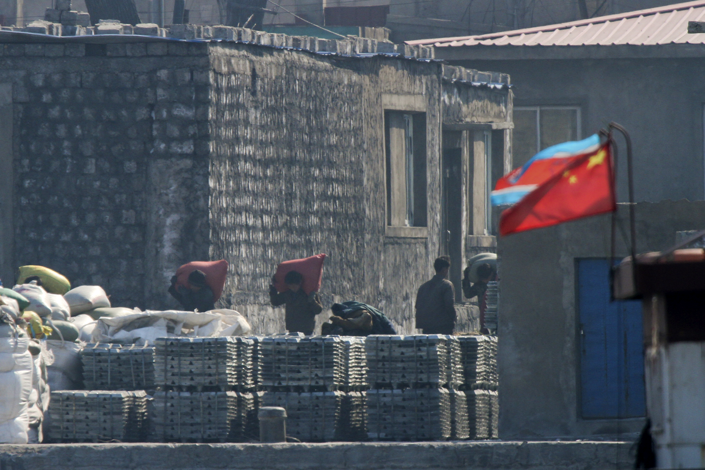 North Koreans load goods on a dockyard with a Chinese and North Korean national flags in Sinuiju, North Korea, as seen from Dandong in northeastern China's Liaoning province. (Chinatopix via AP)