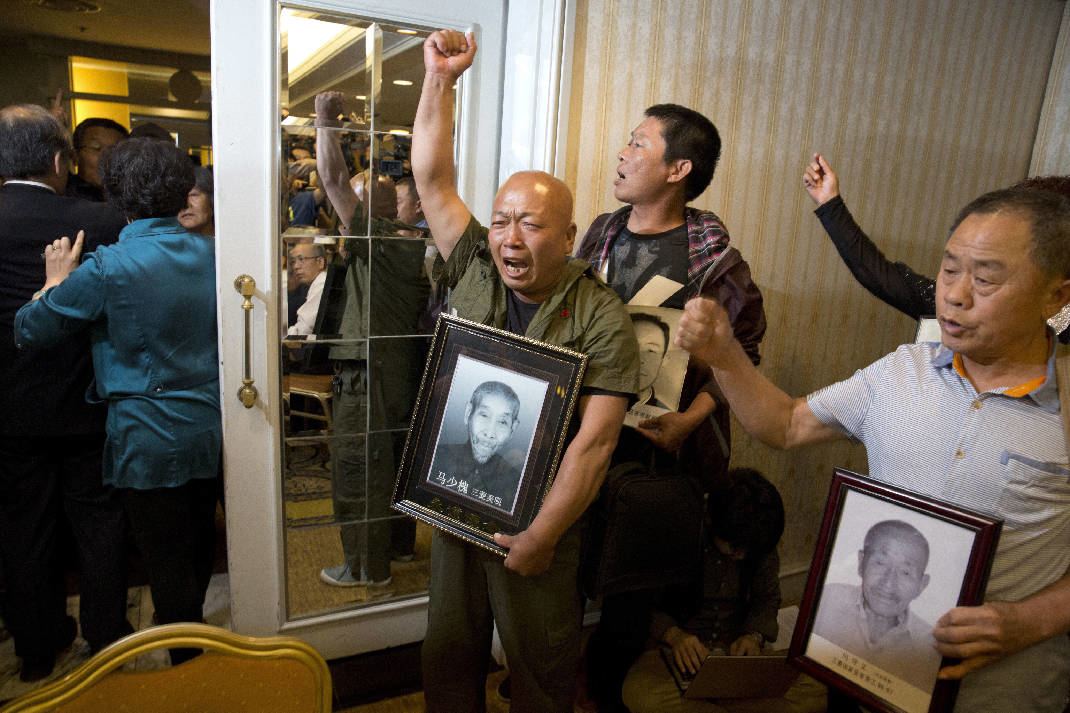 Ma Wenyi, center, holding a photo of his father who was forced to work during World War II at a mine for Mitsubishi Mining Corp., shouts as he demands to join a press conference in Beijing Wednesday, June 1, 2016. (AP Photo/Ng Han Guan)