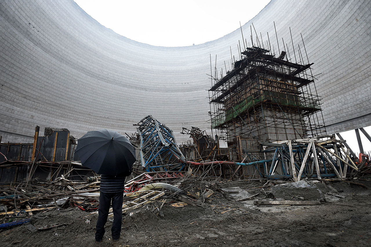 In this Friday, Nov. 25, 2016 photo, a man holding an umbrella looks at the collapsed construction site of a cooling tower for a coal-fired power plant in Fengcheng in central China's Jiangxi province. Chinese authorities have detained nine executives responsible for a power plant accident where an under-construction cooling tower collapsed and killed more than dozen workers. State media reported Monday, Nov. 28 that those under detention included the board chairman of engineering firm Hebei Yineng, which has a history of workplace deaths in its plant projects. (Chinatopix via AP)