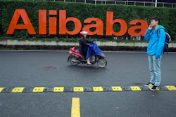 In this Friday, May 27, 2016, file photo, a man talks on his phone as a woman rides on an electric bike past a company logo at the Alibaba Group headquarters in Hangzhou in eastern China's Zhejiang province. Ford Motor Co. is collaborating with Chinese e-commerce giant Alibaba Group to further expand into the world’s largest auto market. The carmaker signed a three-year agreement that will investigate ways to use technology for marketing, sales, cloud computing, and distribution strategies. It hopes to better incorporate digital technologies and platforms into its vehicles. (AP Photo/Ng Han Guan, File)