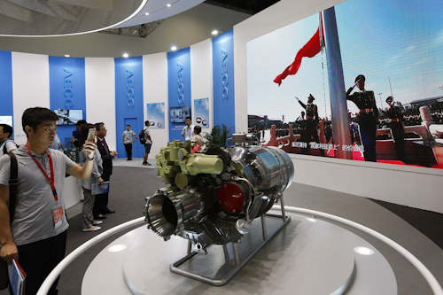 In this Sept. 20, 2017, photo, visitors look at aircraft component parts on display near a screen showing the China's flag raising ceremony, at Aviation Expo China in Beijing. Image credit: AP Photo/Andy Wong