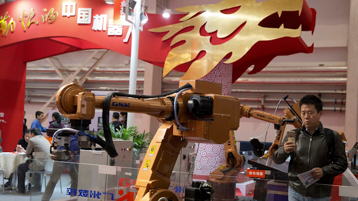 In this Oct. 21, 2016 file photo, visitors look at industrial robots displayed beneath the words that read 'Chinese Robots' during the World Robot Conference in Beijing. Image credit: AP Photo/Ng Han Guan, File