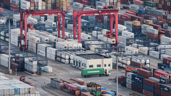 In this March 29, 2018 photo, a cargo truck drives amid stacked shipping containers at the Yangshan port in Shanghai. Image credit: AP Photo/File