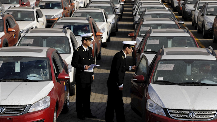 In this Jan. 14, 2015 photo, Chinese customs officials inspect cars being loaded for export at a port in Qingdao in eastern China's Shandong province. Image credit: Chinatopix via AP