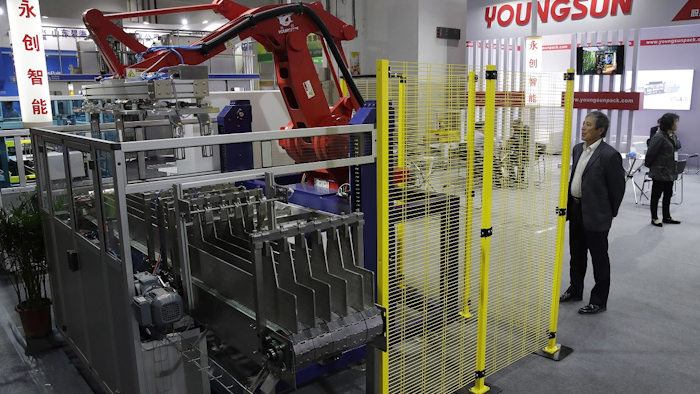 In this April 12, 2018, photo, a visitor watches a Chinese company displaying a Chinese-made industrial robot demonstration on processing soybean at the International soybean exhibition in Shanghai. Image credit: AP Photo/Andy Wong