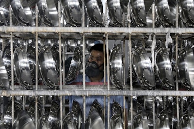 In this Monday, June 25, 2018, photo, a man inspects cooking woks in a factory in Hangzhou in east China's Zhejiang province. Image credit: Chinatopix via AP