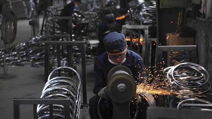 In this June 4, 2018, photo, a worker wields steel wheel rims at a factory in Hangzhou in east China's Zhejiang province. Image credit: Chinatopix via AP