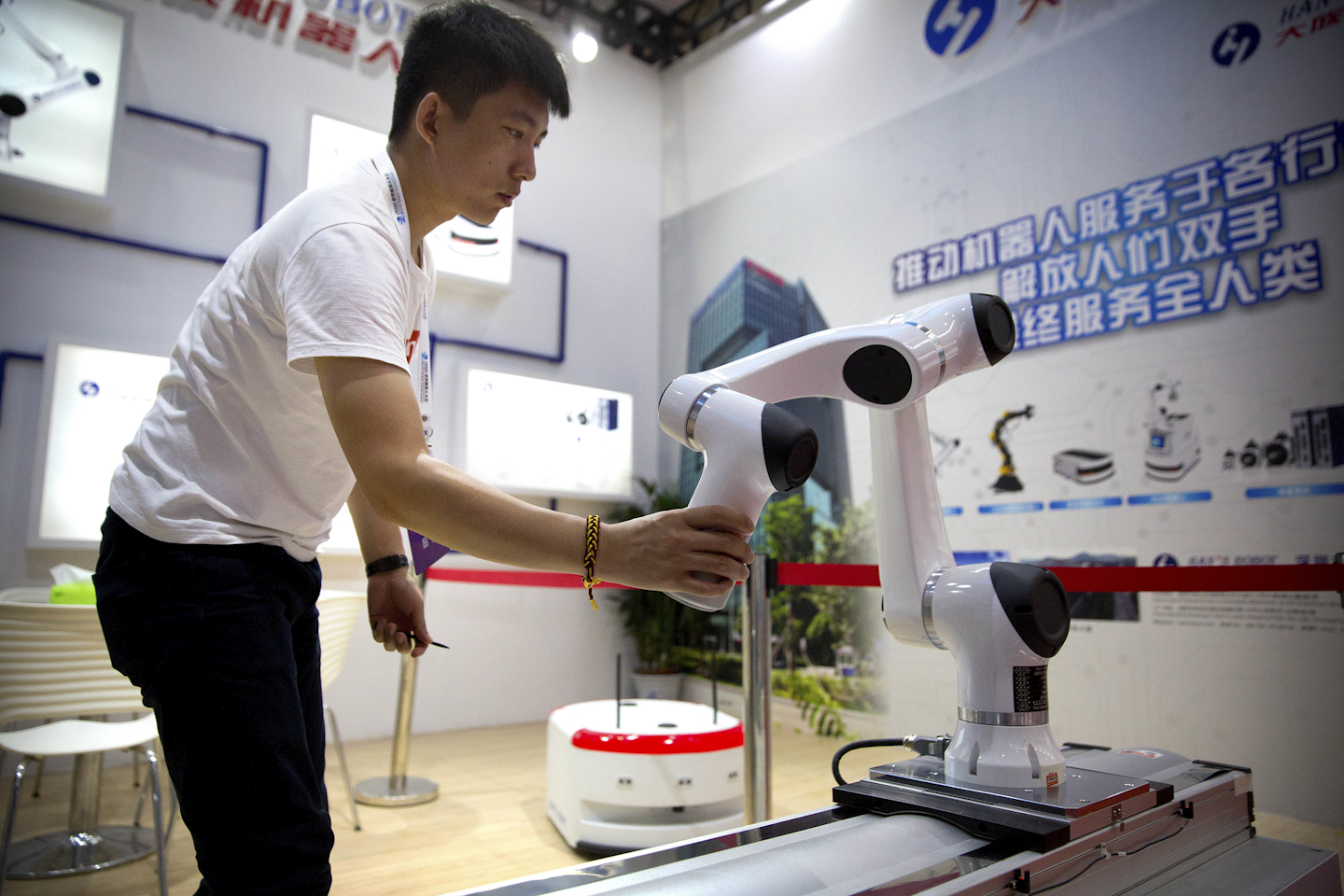 In this Aug. 15, 2018, photo, a visitor looks at a robotic manufacturing arm from Chinese robot maker Han's Robots at the World Robot Conference in Beijing. The head of China's patent and copyright agency is defending what he says are gains in fighting violations - once a chronic complaint by China's trading partners - in a new effort to defuse a tariff war with Washington. (AP Photo/Mark Schiefelbein)