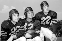 In this Aug. 25, 1948, file photo, veteran quarterback Sid Luckman, center, poses with two newcomers to the Chicago Bears, Johnny Lujack, left, and, Bobby Layne, during preseason football workouts at Collegeville, Ind. Helmets have evolved from the original hard leather of the NFL’s infancy to hard polycarbonate single-piece shells with various amounts of padding and air bladders that served as the primary form of head protection into the beginning of this century.