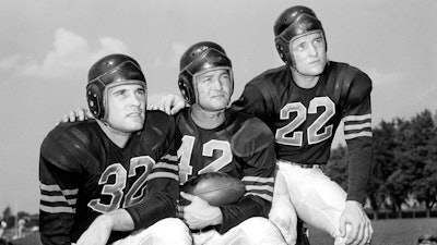 In this Aug. 25, 1948, file photo, veteran quarterback Sid Luckman, center, poses with two newcomers to the Chicago Bears, Johnny Lujack, left, and, Bobby Layne, during preseason football workouts at Collegeville, Ind. Helmets have evolved from the original hard leather of the NFL’s infancy to hard polycarbonate single-piece shells with various amounts of padding and air bladders that served as the primary form of head protection into the beginning of this century.