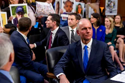In this Oct. 29, 2019, file photo Boeing Company President and Chief Executive Officer Dennis Muilenburg, right foreground, watches as family members hold up photographs of those killed in the Ethiopian Airlines Flight 302 and Lion Air Flight 610 crashes during a Senate Committee on Commerce, Science, and Transportation hearing on Capitol Hill.