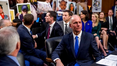 In this Oct. 29, 2019, file photo Boeing Company President and Chief Executive Officer Dennis Muilenburg, right foreground, watches as family members hold up photographs of those killed in the Ethiopian Airlines Flight 302 and Lion Air Flight 610 crashes during a Senate Committee on Commerce, Science, and Transportation hearing on Capitol Hill.