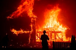 In this Nov. 8, 2018 file photo, a home burns as a wildfire called the Camp Fire rages through Paradise, Calif. Pacific Gas and Electric says it has reached a $13.5 billion settlement that will resolve all major claims related to devastating wildfires blamed on its outdated equipment and negligence. The settlement, which the utility says was reached Friday, Dec. 6, 2019, still requires court approval.
