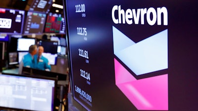 This Oct. 8, 2019, file photo shows the logo for Chevron on the floor of the New York Stock Exchange. Chevron Corp. reports financial results Friday, Nov. 1. Chevron said Tuesday, Dec. 10, it will book a charge of at least $10 billion because lower long-term prices for oil and natural gas are making some projects less valuable.