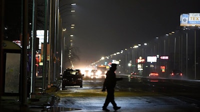 In this May 2, 2019, file photo, a pedestrian crosses Gratiot Street at Outer Drive East under a bright streetlight flanked by dimmer streetlights in Detroit. Leotek Electronics USA has agreed to pay $4 million to settle a lawsuit with Detroit over thousands of defective streetlights in Detroit, a newspaper reported. The city sued the company last spring, alleging that roughly 20,000 lights were failing.