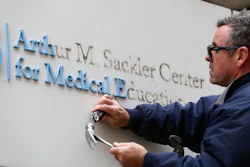 Worker Gabe Ryan removes a sign that includes the name Arthur M. Sackler at an entrance to Tufts School of Medicine, Thursday, Dec. 5, 2019, in Boston. Tufts University says it is stripping the Sackler name from its campus in recognition of the family's connection to the opioid crisis.