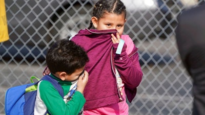 Children covering their noses and mouths leave school where multiple people were treated for jet fuel exposure at Park Avenue Elementary School in Cudahy, Calif., on Tuesday, Jan. 14, 2020. A jet returning to LAX dumped its fuel over the neighborhood and the school. Affected people at the school were treated for skin and eye irritation. No patients were transported to hospitals.