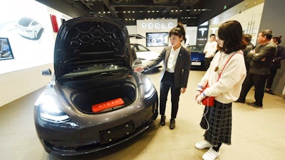 In this Nov. 24, 2019, photo, a saleswoman talks about a Tesla Model 3 car at a Tesla showroom in Hangzhou in eastern China's Zhejiang Province. Tesla's Shanghai factory delivered its first cars to customers Monday, Jan. 6, 2020, and chief executive Elon Musk said the electric automaker plans to set up a design center in China to create a model for worldwide sales.