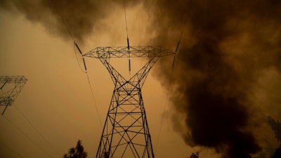 In this Nov. 9, 2018, file photo, smoke billows around power transmission lines as the Camp Fire burns in Big Bend, Calif. Pacific Gas & Electric Co., the nation's largest electric utility, filed for bankruptcy last year after facing an estimated $50 billion in damages from several Northern California wildfires that were linked to its equipment, including one blaze in 2018 that killed 85 people and destroyed about 19,000 buildings.