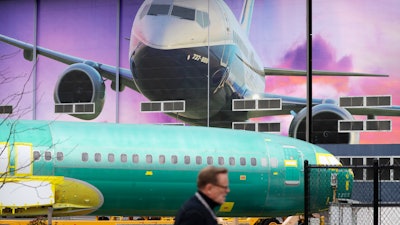 In this Dec. 16, 2019 file photo, a Boeing worker walks past a 737 model fuselage and a giant mural of a jet on the side of the manufacturing building behind in Renton, WA.