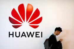 In this Oct. 31, 2019, file photo, a man uses his smartphone as he stands near a billboard for Chinese technology firm Huawei at the PT Expo in Beijing.