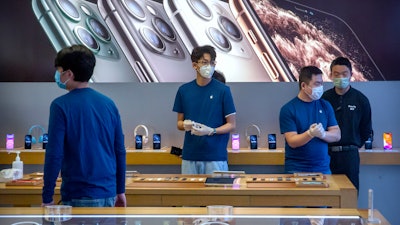 In a Feb. 14, 2020 file photo, employees wear face masks as they stand in a reopened Apple Store in Beijing. Apple Inc. is warning investors that it won't meet its second-quarter financial guidance because the viral outbreak in China has cut production of iPhones.