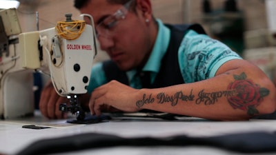 In this Feb. 13, 2020 photo, an employee, donning a tattoo with a motto reads in Spanish: 'Only God can judge me,' stitches shoe components at the Tenis Court factory, in Leon, Guanajuato state, Mexico. Part of Guanajuato’s odd reality stems from its success at cracking down on crimes that impact businesses together with its inability to stop the drug gang war.