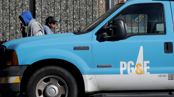 In this photo taken Feb. 18, 2020, people walk behind a Pacific Gas and Electric truck parked in San Francisco.