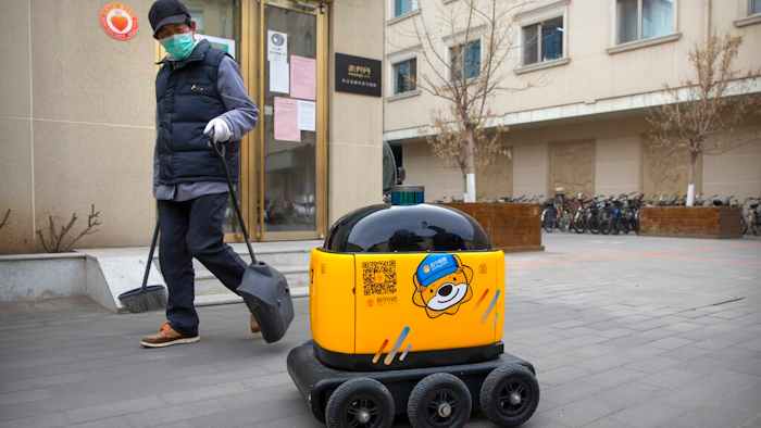In this March 18, 2020, photo, a maintenance worker looks at a robot outside the offices of ZhenRobotics in Beijing. While other industries struggle, one robot maker says China's virus outbreak is boosting demand for his knee-high, bright yellow robots to deliver groceries and patrol malls for shoppers who fail to wear masks.