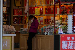 In this Tuesday, March 10, 2020, a staff wearing a protective mask browses her smartphone while waiting for customers at a shop at the Wangfujing shopping district following the coronavirus outbreak in Beijing.