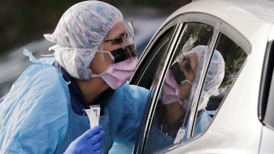 In this March 17 photo, Laurie Kuypers, a registered nurse, reaches into a car to take a nasopharyngeal swab from a patient at a drive-through COVID-19 coronavirus testing station for University of Washington Medicine patients in Seattle.