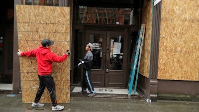 Phu Dang, left, the owner of i5 Pho restaurant, gets help from a contractor as he boards up his business, Monday, March 30, 2020, in Seattle's downtown Pioneer Square neighborhood.
