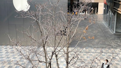 A woman wearing mask walks past the Apple store in an empty mall district in Beijing, China on Wednesday, Feb. 26, 2020. The tech giant Apple has reopened some of its stores in China but says the viral outbreak is starting to disrupt its supplies.