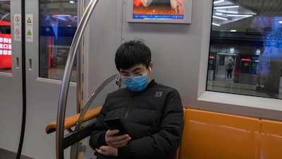 A passenger sits under a public information display encouraging the use of mask on a subway train in Beijing Monday, March 9, 2020. With almost no new COVID-19 cases being reported in Beijing, workers are slowly returning to their offices with masks on and disinfectant in hand. But officials remain cautious, torn between wanting to restart the economy and fear of a resurgence of the outbreak.