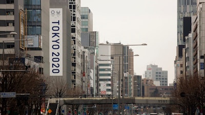In this March 4, 2020, file photo, a large Tokyo 2020 Olympic banner hangs on the facade of a building in Tokyo. The tentacles of cancelling the Tokyo Olympics — or postponing or staging it in empty venues — would reach into every corner of the globe, much like the spreading virus that now imperils the opening ceremony on July 24.