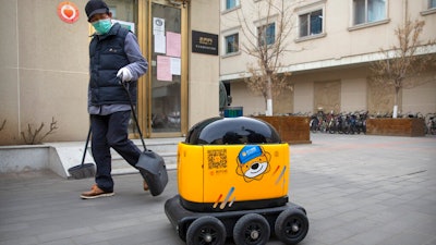 In this March 18, 2020, photo, a maintenance worker looks at a robot outside the offices of ZhenRobotics in Beijing. While other industries struggle, one robot maker says China's virus outbreak is boosting demand for his knee-high, bright yellow robots to deliver groceries and patrol malls for shoppers who fail to wear masks.