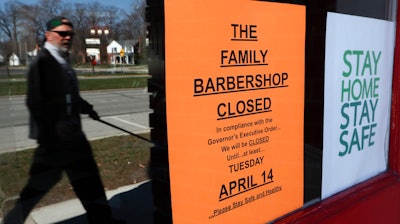 A pedestrian walks by The Family Barbershop, closed due to a Gov. Gretchen Whitmer executive order, in Grosse Pointe Woods, Mich., Thursday, April 2, 2020.