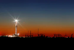 In this Thursday, April 2, 2020 photo, an oil rig lights up the horizon on the outskirts of Midland, Texas after a late sunset.