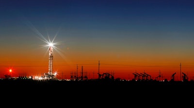 In this Thursday, April 2, 2020 photo, an oil rig lights up the horizon on the outskirts of Midland, Texas after a late sunset.