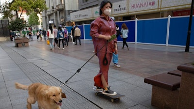 A resident gets a ride from her dog along a retail street in Wuhan in central China's Hubei province, Thursday, April 9, 2020. Released from their apartments after a 2 1/2-month quarantine, residents of the city where the coronavirus pandemic began are cautiously returning to shopping and strolling in the street but say they still go out little and keep children home while they wait for schools to reopen.