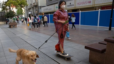 A resident gets a ride from her dog along a retail street in Wuhan in central China's Hubei province, Thursday, April 9, 2020. Released from their apartments after a 2 1/2-month quarantine, residents of the city where the coronavirus pandemic began are cautiously returning to shopping and strolling in the street but say they still go out little and keep children home while they wait for schools to reopen.