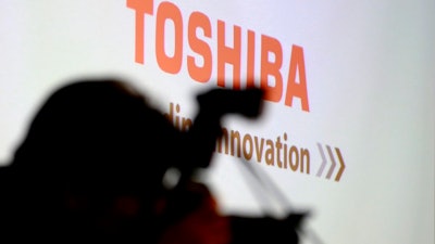 In this April 11, 2017 file photo, a photographer takes a photo before a press conference at the Toshiba Corp.'s headquarters in Tokyo. Toshiba and a consortium led by Bain Capital Private Equity signed a deal Thursday for the sale of the Japanese electronics company's computer memory chip business, a move long opposed by Toshiba's U.S. joint venture partner Western Digital.