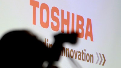 In this April 11, 2017, file photo, a photographer is silhouetted before a press conference at the Toshiba Corp. headquarters in Tokyo. Troubled Toshiba Corp. is selling 95 percent of its TV and other visual products subsidiary to Chinese electronics maker Hisense Group. Toshiba, which needs to sell parts of its business to survive, announced the 12.9 billion yen ($113 million) deal Tuesday, Nov. 14, 2017. It’s set to be completed by or after February 2018, pending regulatory approval and other steps.