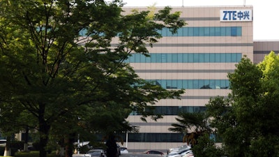 In this April 17, 2018, photo, a woman walks through the parking lot of a building hosting ZTE subsidiaries in Nanjing in eastern China's Jiangsu province. Chinese tech company ZTE said Friday, April 20, 2018, that it won't accept an 'unfair' U.S. penalty in a case involving exports of telecoms equipment to North Korea and Iran and is seeking a solution through legal channels.