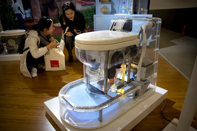 Visitors look at a model of a self-contained toilet at the Reinvented Toilet Expo in Beijing, Tuesday, Nov. 6, 2018. With a jar of human feces on a podium next to him, billionaire philanthropist Bill Gates has kicked off a 'Reinvented Toilet' Expo in China. Gates said Tuesday that the technologies on display at the three-day expo in Beijing represent the most significant advances in sanitation in nearly 200 years.