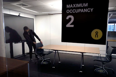 In this Thursday, May 7 photo, Vice President Rachel Zsembery at the design firm Bergmeyer, positions chairs in a conference room with a designated maximum occupancy of two people, at the firms offices, in Boston. Out of concern for the coronavirus Bergmeyer is restructuring the way its workspace is used, including reinstalling dividers on 85 desks at its Boston office that had been removed over the years.