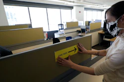 This Thursday, May 7 photo shows Interior Designer Stephanie Jones at the design firm Bergmeyer putting up a safe distancing reminder indicating one way foot traffic to a cubicle at the firms offices in Boston.