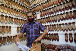 A shopkeeper dusts footwear after opening his shop after weeks, at a market area in Jammu, India